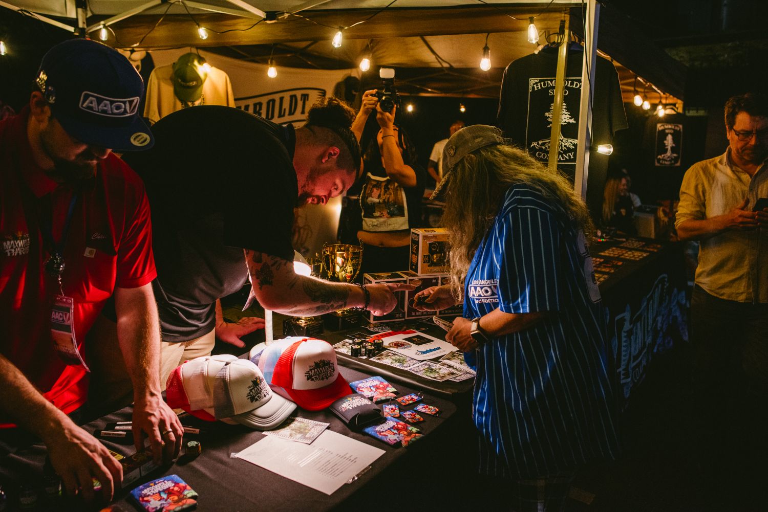 Attendees browsing trucker hats and merchandise at the Maxwell Pharms vendor booth during the AAC 2065 cannabis expo